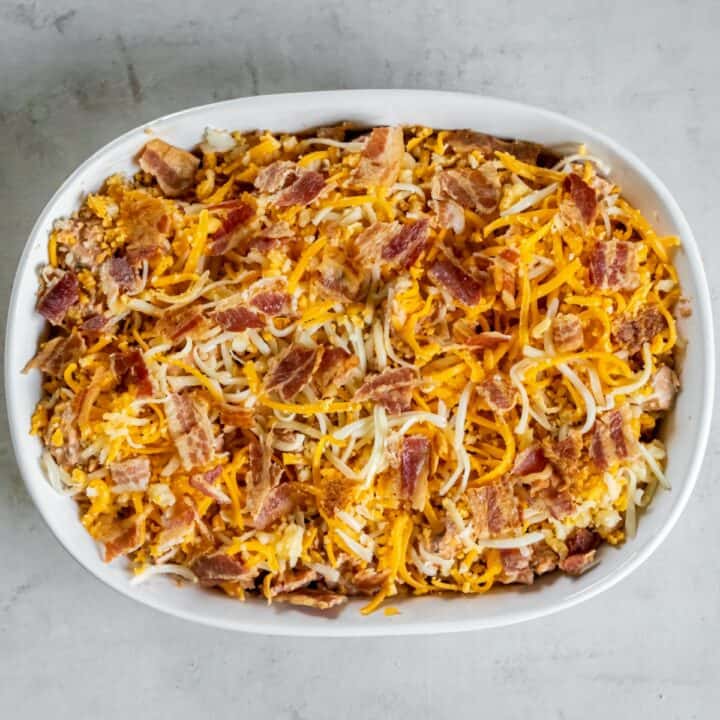 Fully prepared keto BBQ chicken casserole topped with shredded cheese and bacon in a casserole dish ready to be baked.