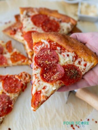 A hand picking up a slice of pepperoni pizza topped with herbs.