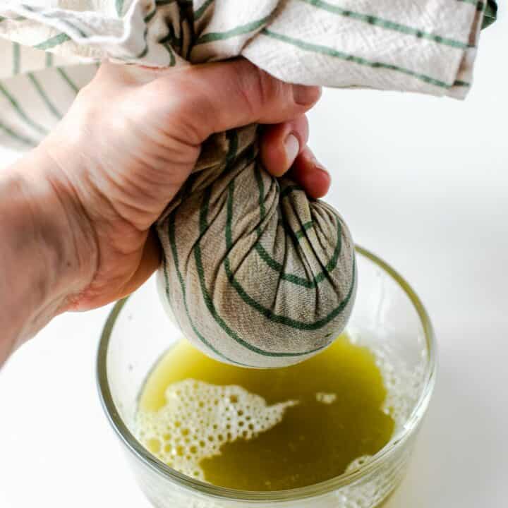 Thawed frozen spinach in a kitchen towel with the water being wrung out over a glass bowl.