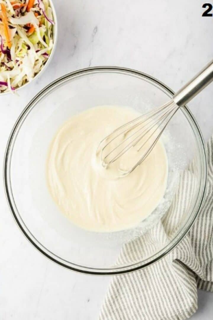 The coleslaw dressing being whisked in a glass bowl.