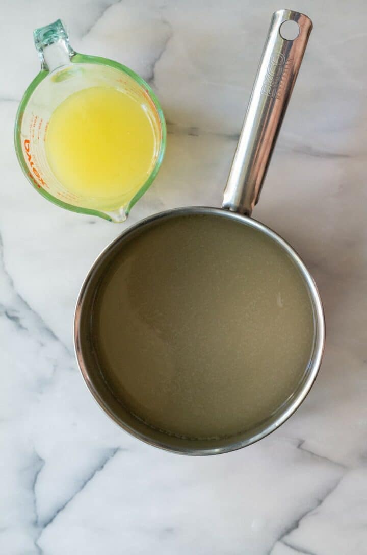 Water and sugar free sweetener in a medium size pot next to a measuring cup of lemon juice.