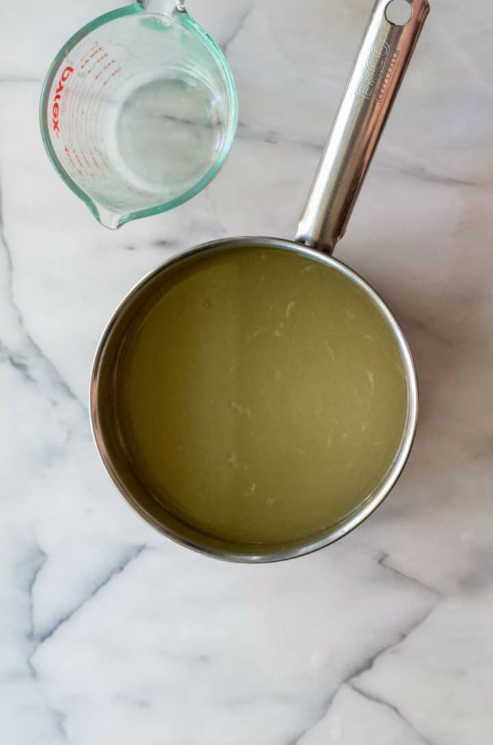 Keto lemonade fully mixed in a medium size pot next to an empty measuring glass.