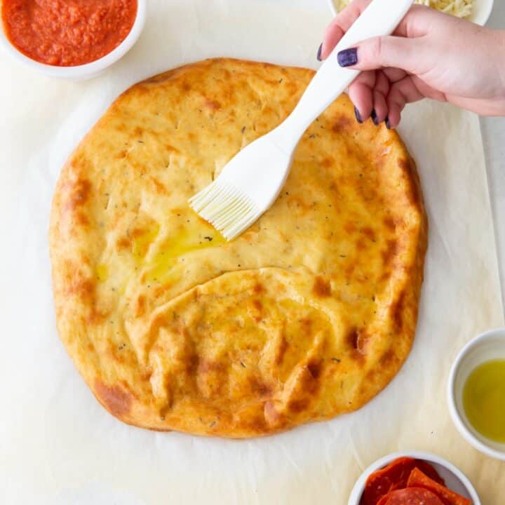 Baked keto pizza crust being brushed with olive oil.