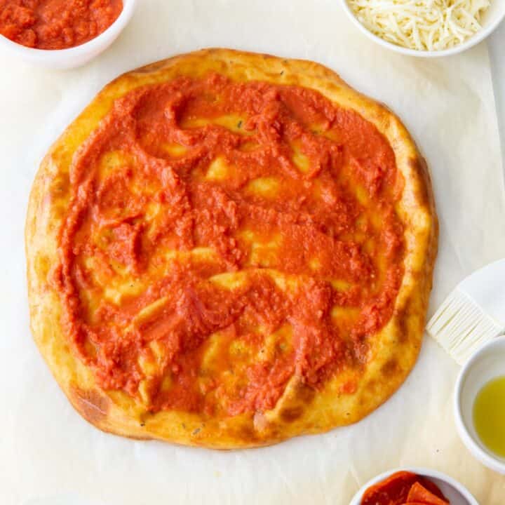 Pizza crust topped with a layer of pizza sauce.