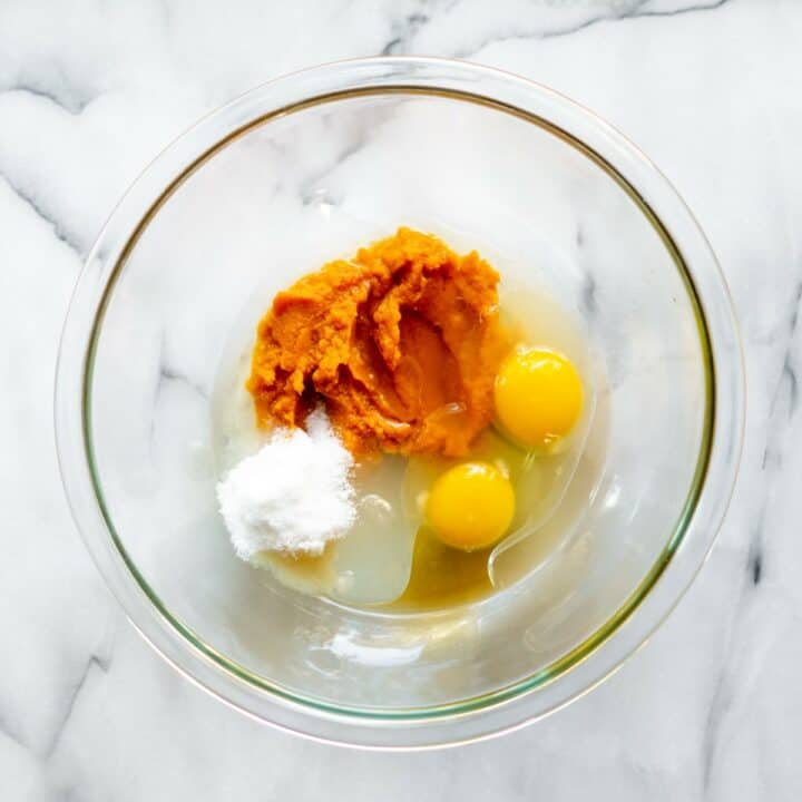 The ingredients, pumpkin, oil, sweetener, eggs and vanilla extract in a glass mixing bowl.