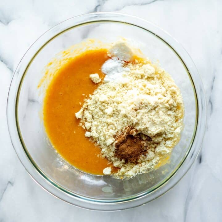 Glass bowl with the almond flour, pumpkin spice, salt and baking soda being added to the wet ingredients.