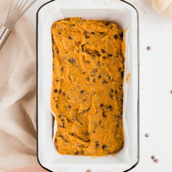 Parchment lined loaf pan filled with pumpkin bread batter.