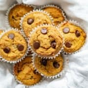 low carb pumpkin muffins with chocolate chips on a white dish towel in a bowl.