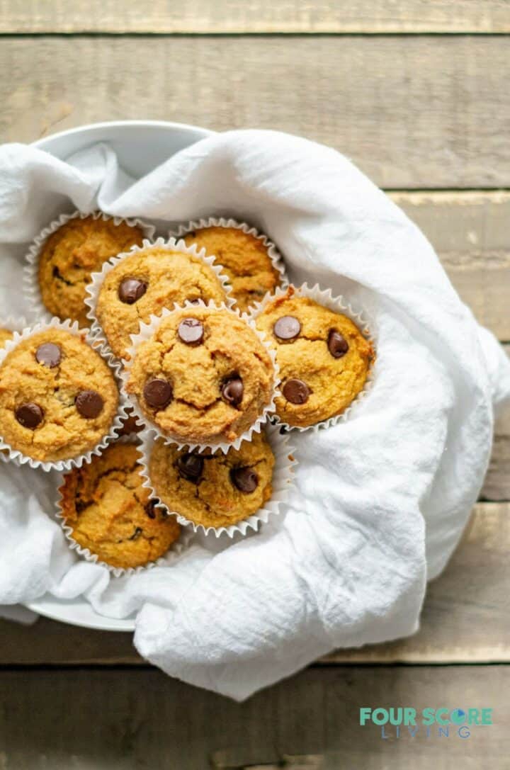 low carb pumpkin muffins with chocolate chips on a white dish towel in a bowl.