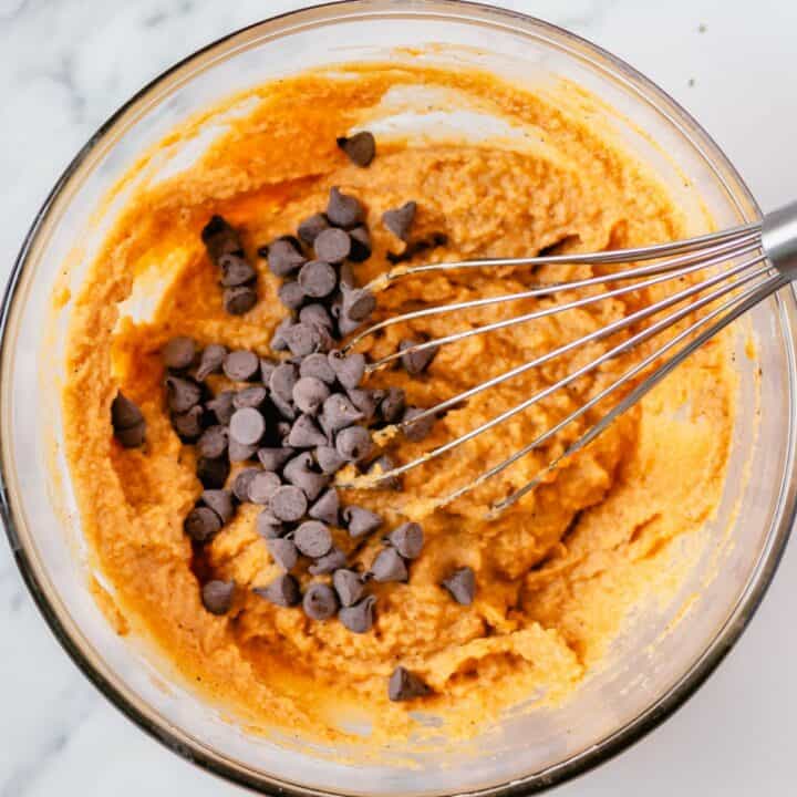 Sugar free chocolate chips being added to the pumpkin muffin batter in a glass bowl.