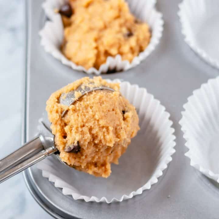 Pumpkin batter being spooned into paper liners in a muffin pan.