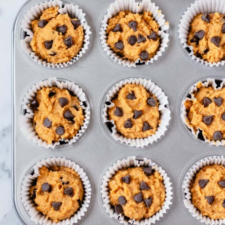 Nine unbaked pumpkin muffins topped with chocolate chips in a muffin pan.