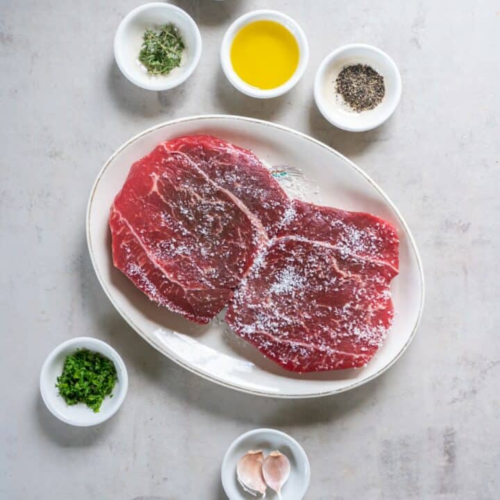 Plate with heavily salted steaks surrounded by remaining ingredients in individual bowls.