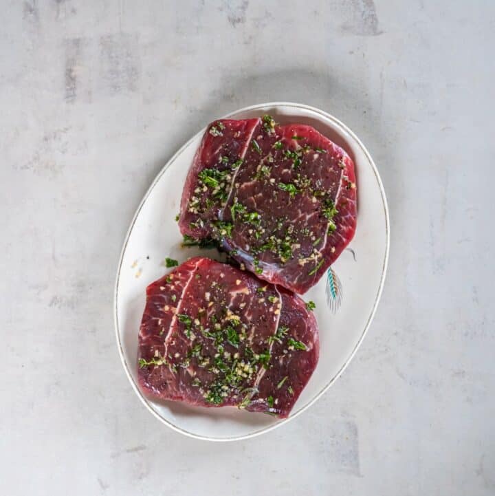 Plate with two steaks coated in the fresh herb, oil and garlic mixture.