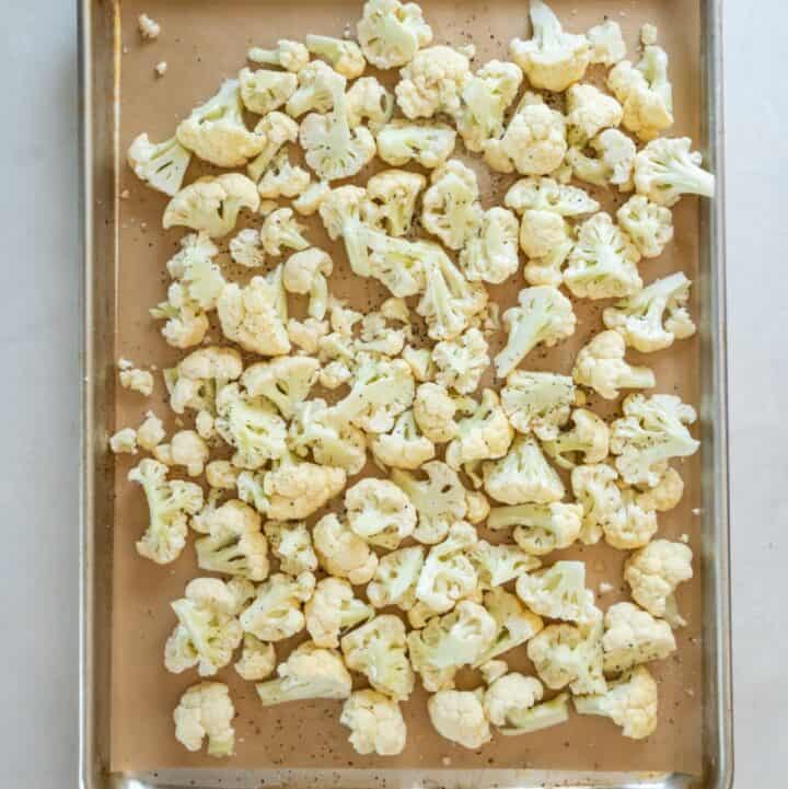 Lined baking sheet with seasoned cauliflower florets ready to bake.