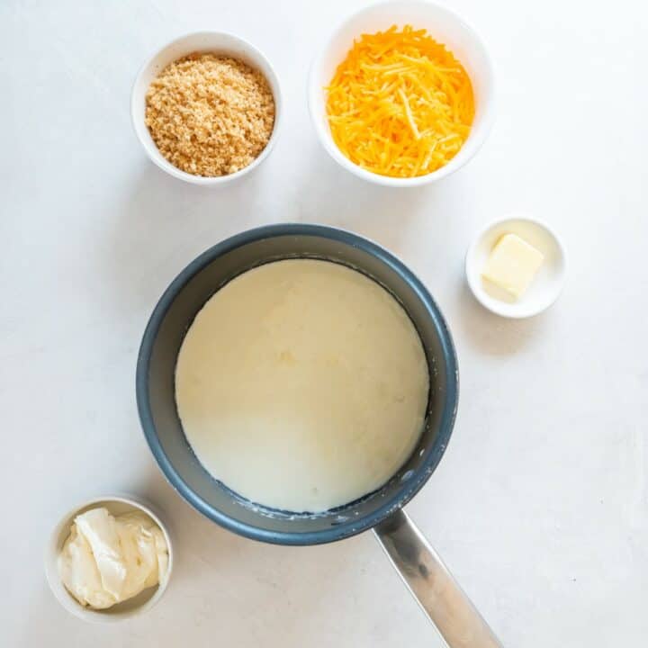 Sauce pan with heavy cream surrounded by individual bowls of cheese, butter and pork rinds.