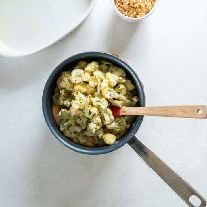 Roasted cauliflower florets being mixed into the sauce in a saucepan.