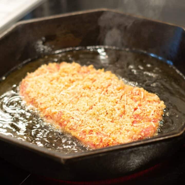 Keto chicken fried steak being fried in oil in a large skillet.