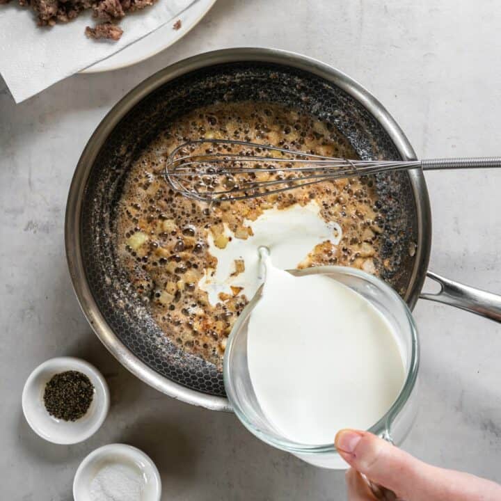 Heavy cream being added to cooked onion and garlic in frying pan.