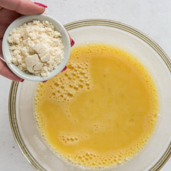 Coconut flour being added to lemon bars mixture in a glass bowl.