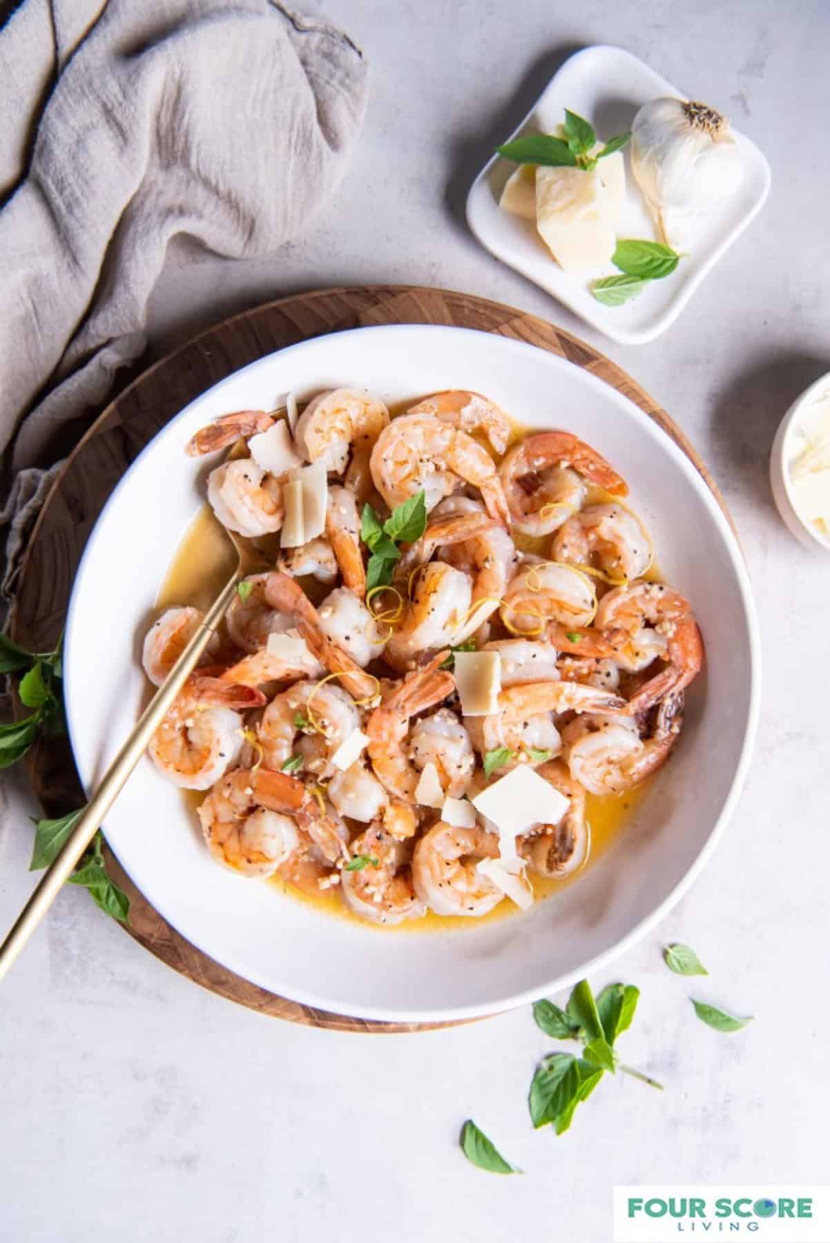 A bowl filled with keto shrimp scampi in a white wine garlic butter sauce garnished with fresh basil leaves and sliced pieces of fresh Parmesan cheese.