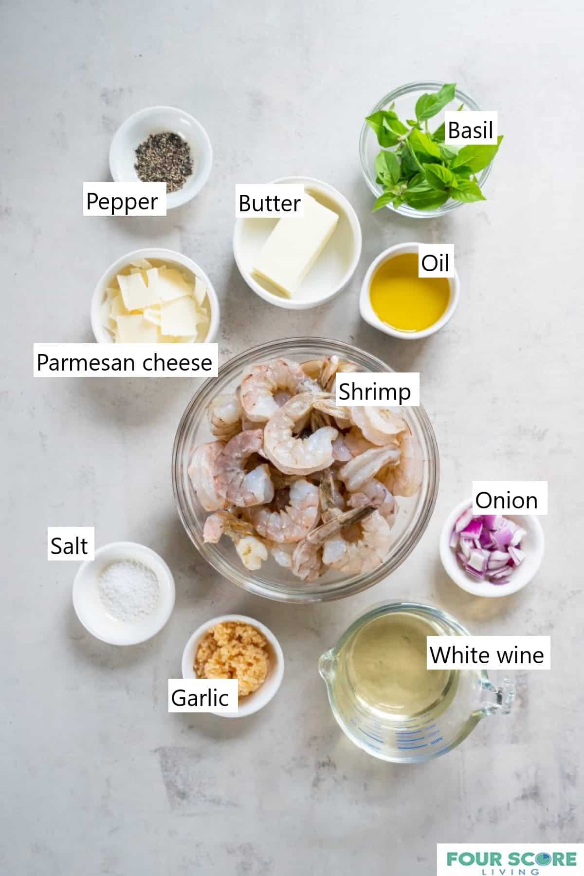 Individual bowls holding the ingredients to make keto shrimp scampi, including avocado oil, a half stick of butter, slices of fresh Parmesan cheese, raw shrimp with tails on, chopped red onion, minced garlic, salt and white wine.