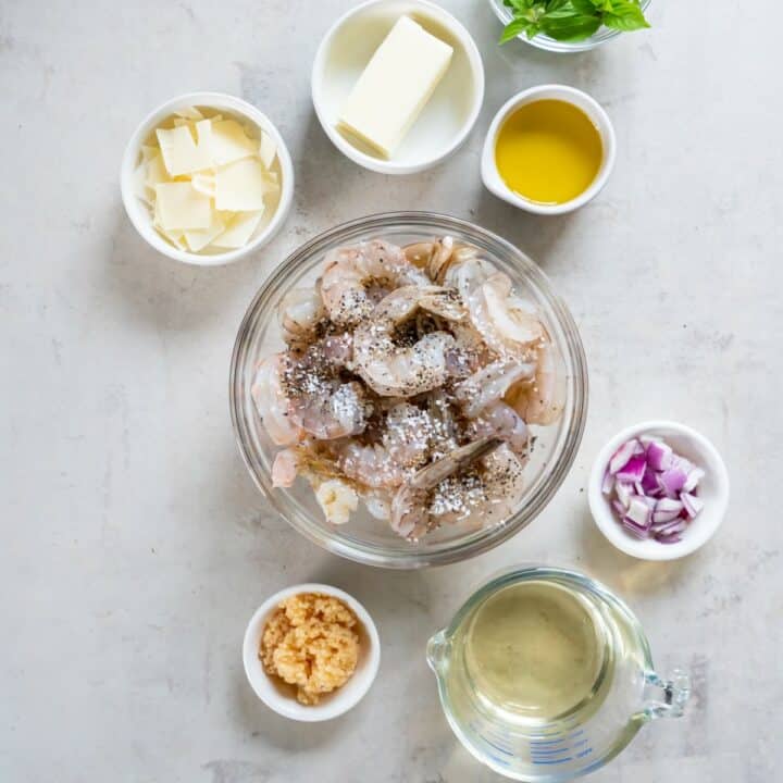 Seasoned shrimp in a glass bowl surrounded by remaining ingredients in individual bowls.