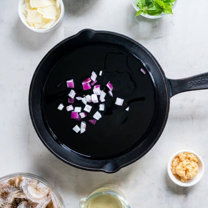 Cast iron skillet with chopped onion being added to hot oil.