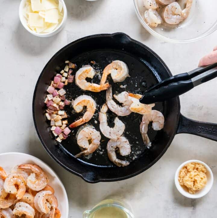 Cast iron skillet with shrimp being cooked. The cooked onion has been pushed to the side of the skillet.