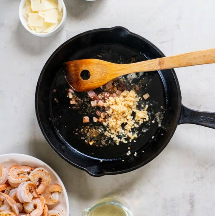 Garlic being added to the cast iron skillet after the cooked shrimp have been removed.