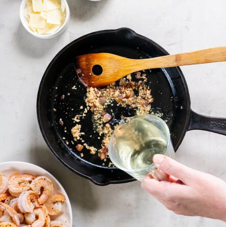 White wine being added to the cooked garlic and onion in the cast iron skillet.