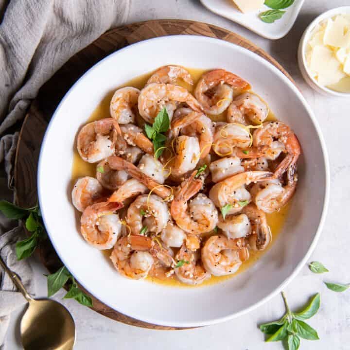 Shrimp and white wine garlic butter sauce in a bowl. Garnished with parmesan cheese and fresh basil.