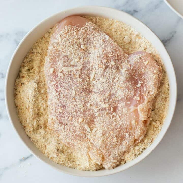 A chicken breast being coated in the breadcrumb / flour mixture.