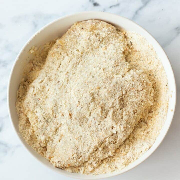 A chicken breasts being coated in the breadcrumb/flour mixture again after being dunked in a bowl of heavy cream.