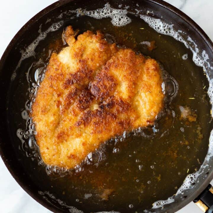 A breaded chicken breast being fried in a oil filled skillet.