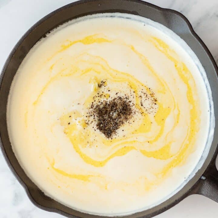 The pasta sauce being made in an iron skillet. It is filled with cream, butter, Italian seasoning, garlic, salt and pepper.