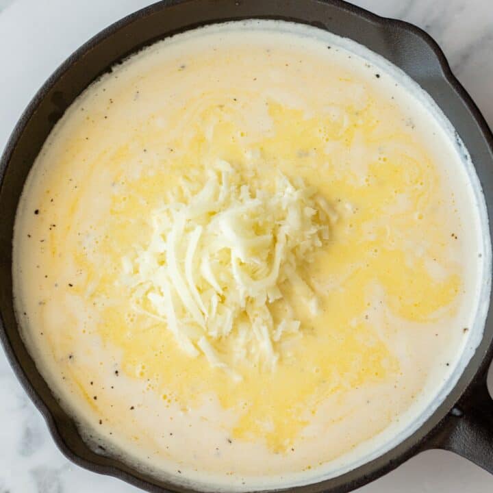 Grated asiago cheese is being added to the pasta sauce cooking in an iron skillet.