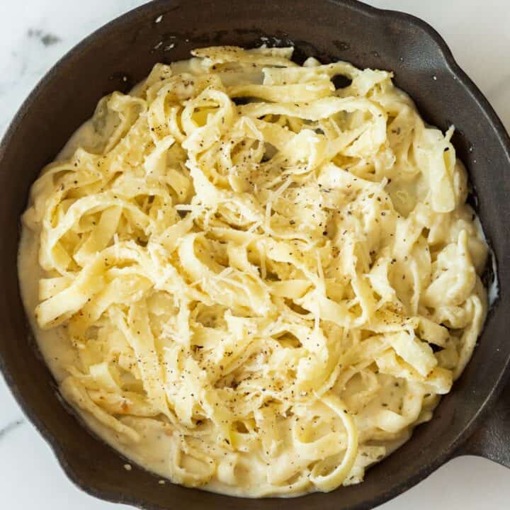 The cooked fettucine has been added to the skillet full of pasta sauce.