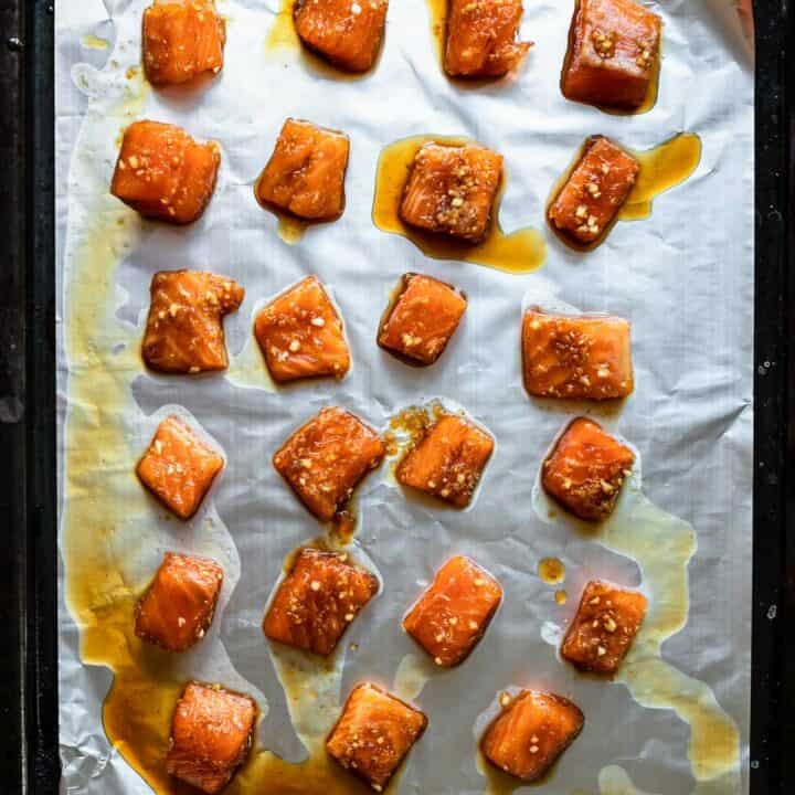 Marinated honey garlic salmon bites on a baking sheet lined with foil ready to be broiled.