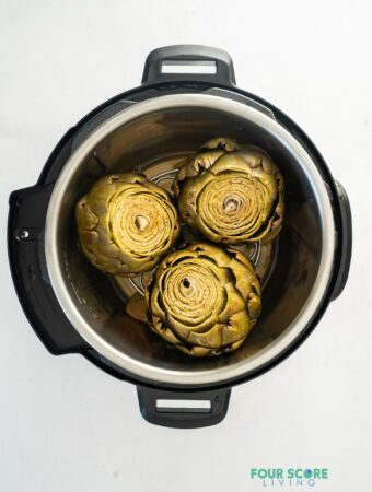 An instant pot, opened, with three cooked artichokes inside.