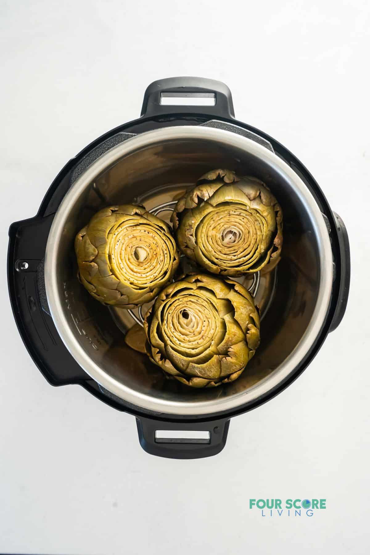 An instant pot, opened, with three cooked artichokes inside.