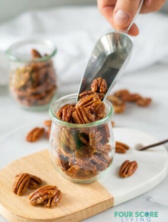 A scoop of keto candied pecans being poured into a small glass jar.