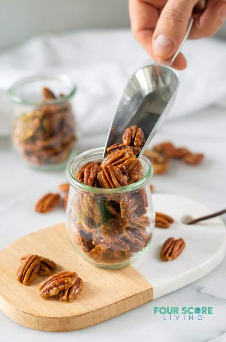 A scoop of keto candied pecans being poured into a small glass jar.