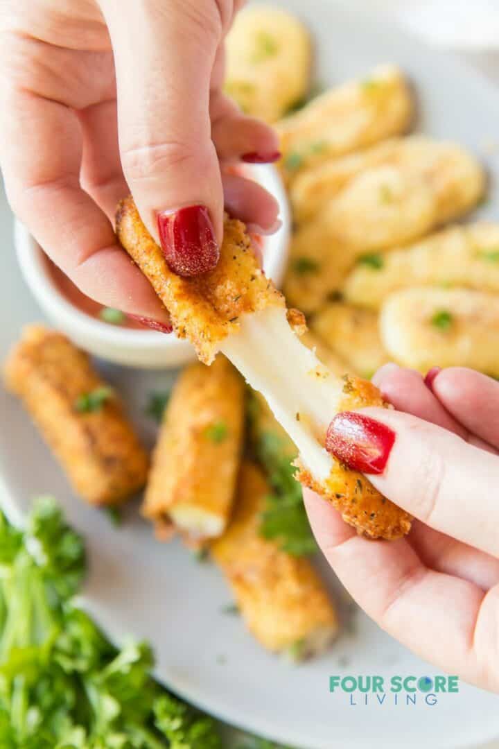 A mozzarella stick being pulled apart to show the melty cheese inside.