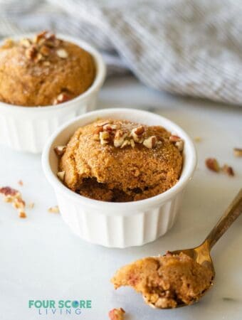 Two keto pumpkin mug cakes in individual ramekins. A spoonful has been taken out of one.