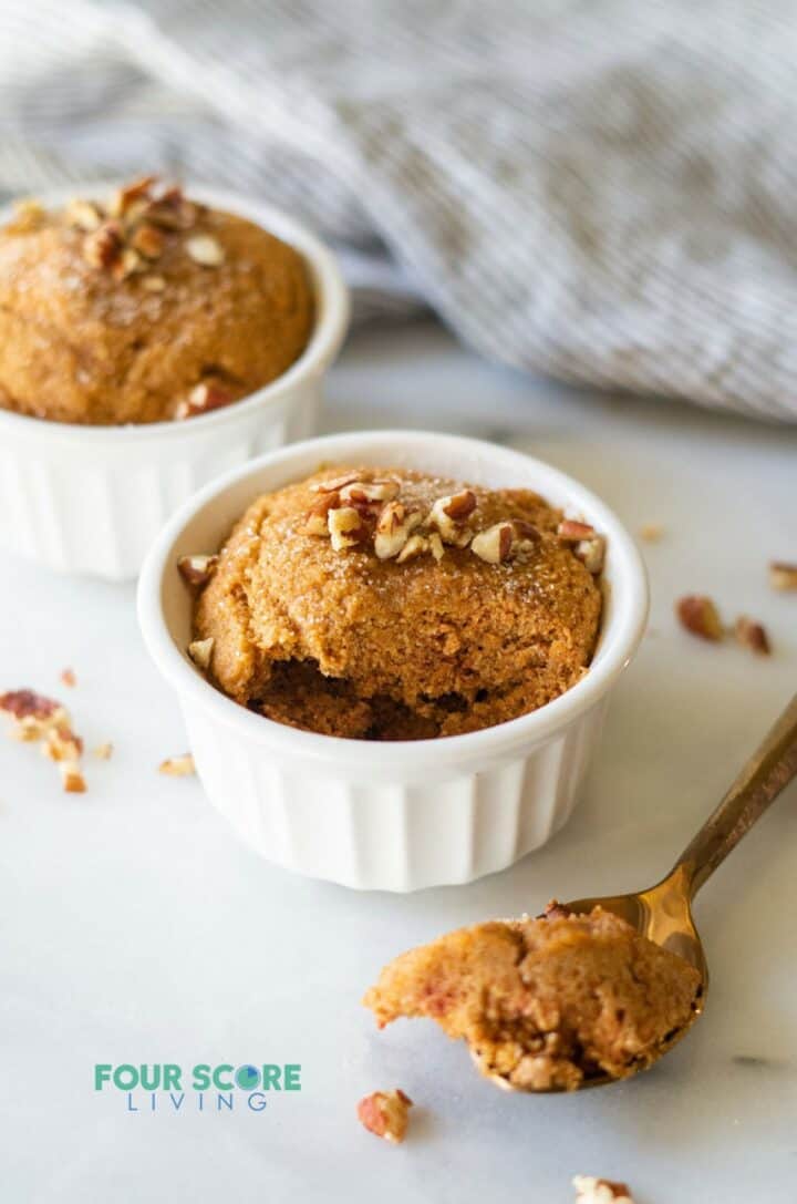 Two keto pumpkin mug cakes in individual ramekins. A spoonful has been taken out of one.