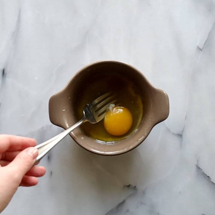 An egg and vanilla extract being added to melted butter in microwave safe mug.