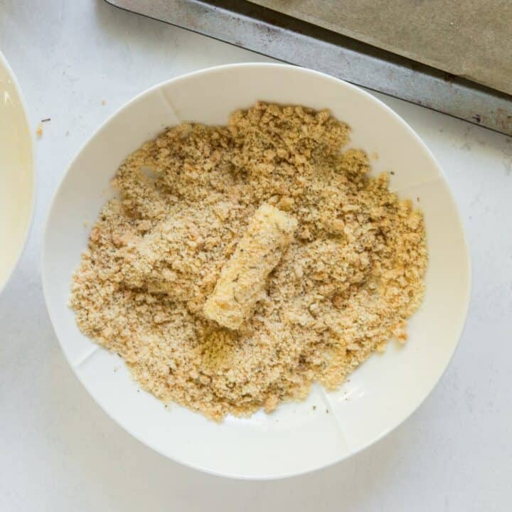 A mozzarella stick being dipped in the seasoned pork rind mixture.