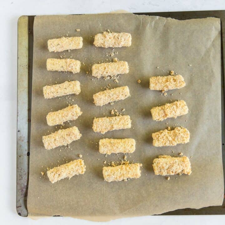 A parchment lined baking sheet with three rows of fully prepared mozzarella sticks ready to be frozen.