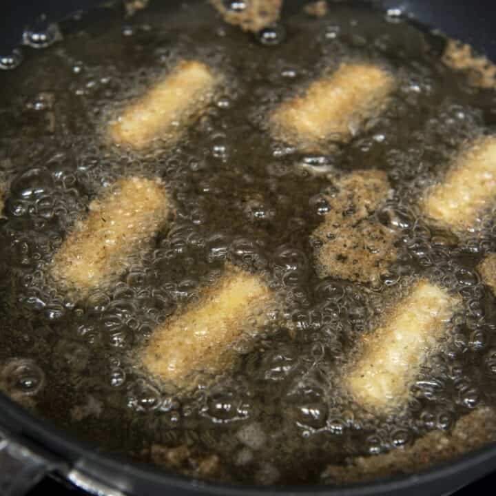 Prepared mozzarella sticks being fried in an oil filled skillet.